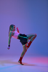 Fototapeta na wymiar Full-length of sportive teen girl, mma fighter in uniform training against purple studio background in neon lights. Concept of mixed martial arts, sport, hobby, competition, athleticism, strength, ad
