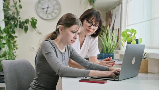 Mother helping preteen daughter to study, looking at laptop at home
