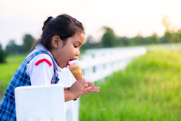 Cute Asian girl in school uniform eating ice cream while on vacation with family, and blured of...