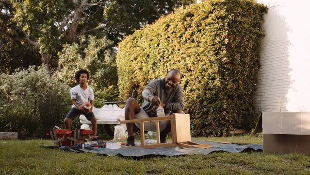 Black father repairing chair with son plays with football in the garden at home
