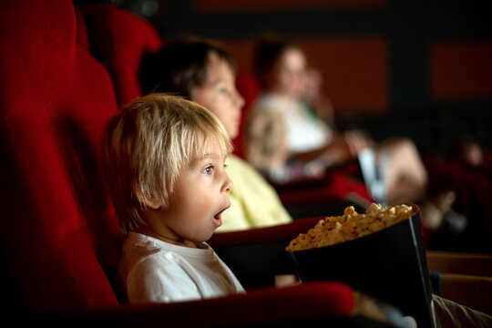 Cute child, boy, watching movie in a cinema, eating popcorn and enjoying