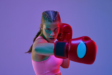 Competitive teen girl, MMA fighter in motion, kicking in gloves against purple studio background in neon lights. Concept of mixed martial arts, sport, hobby, competition, athleticism, strength, ad