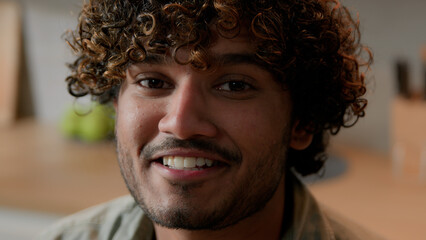 Close up smiling Arabian man homeowner with curly hair vlogger look at camera at kitchen. Portrait Indian male face with smile indoors. Headshot ethnic guy business video conference call web cam view