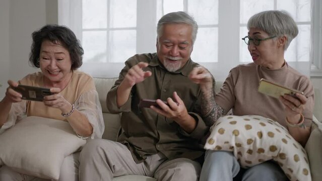 group of old senior retired asian people playing smartphone online game on sofa in living room at nursing home or senior daycare center.activity with smartphone technology concept