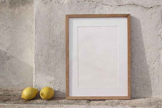 Minimal empty vertical wooden frame picture mockup against white old textured white wall in sunlight. Fresh yellow lemons fruit. Summer background with light, shadows. Mediterranean design.