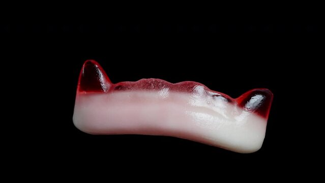 Chewy gummy candy in the shape of red vampire fangs, rotating. Isolated on a black background.