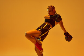 Fototapeta na wymiar Dynamic photo of athletic teen girl, mma fighter in sportswear training against orange background in neon lights. Concept of mixed martial arts, sport, hobby, competition, athleticism, strength, ad