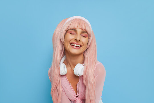 Close upt of beautiful girl dressed like popular doll in pink, smiling with closed eyes on blue studio background, doll trend concept, copy space