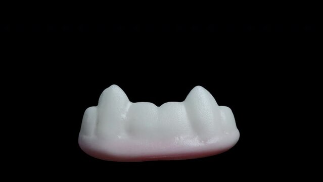 A gummy candy shaped like white teeth and vampire fangs, rotating on a black background, isolated, in a close-up shot.