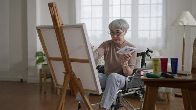 disabled artist senior female drawing sitting on wheel chair at home.small business,entrepreneurship and Home hobby after retirement.Disabled Elderly female in wheelchair at art studio