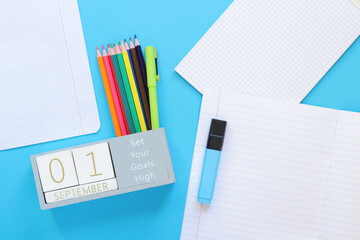 01 September. Image of a wooden calendar for September 1 on a blue table, top view. Back to school. Calendar, pencils and an open notebook. Stationery items. Copy space