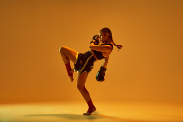 Leg kick. Sportive teen girl, mma fighter athlete in motion, training, fighting against orange...