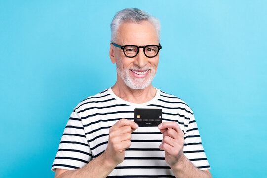 Photo portrait of handsome grandad specs hold credit card money ecommerce dressed stylish striped clothes isolated on blue color background