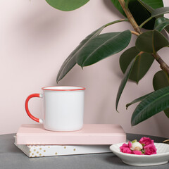 White mug mockup with books and accessories on a table and a ficus plant. White red blank cup for your design. Empty mockup template