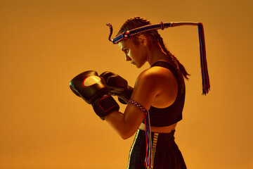 Defense position. Teen girl, concentrated MMA athlete in boxing gloves training against orange...