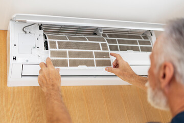 Senior man cleaning air conditioner, remove dirty filter at home. Ventilation, fresh air concept