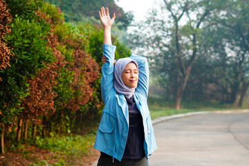 Beautiful Muslim woman working out outdoors in the morning. Sporty woman with a hijab warming up by doing stretch exercises.