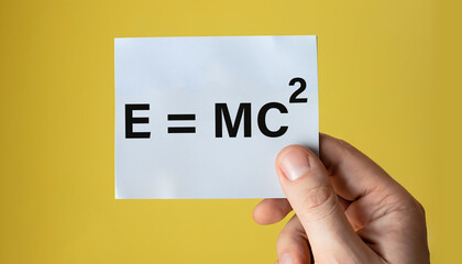 E =MC2 displayed on hand holding paper isolated on lite yellow background. 