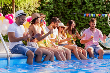 Friends sitting by poolside and drink beers while listening music