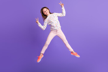 Fototapeta na wymiar Full length photo of pretty friendly small girl wear dotted sweater jumping high showing two v-signs isolated violet color background