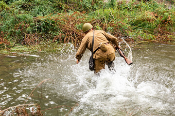 WW II historical reenactment.  A Soviet infantry soldier crossing the river during an attack. View from the back