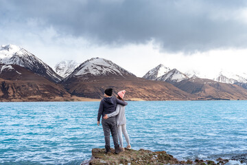 Asian couple posing with the beautiful scenic view of Lake Pukaki east bank, with their mesmerizing...
