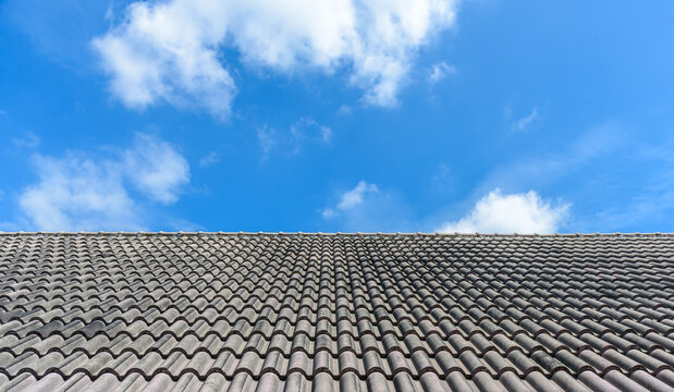 Black tile roof of house under blue sky and white cloud, tiles background, exterior building design. Roof tiles close up image.