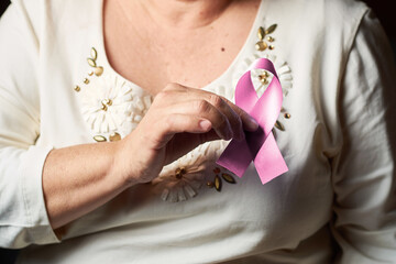 Hands of middle aged woman holds pink ribbon, on breast cancer day. Breast cancer awareness.