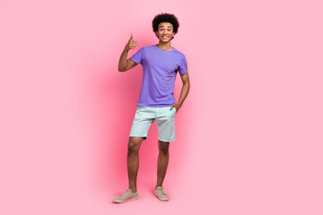 Full length photo of cool man with afro hairstyle dressed blue t-shirt arm in pocket showing thumb up isolated on pink color background