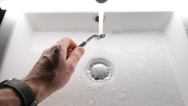 Cleaning shaving razor in bathroom sink. Rinsing off razor with water.
