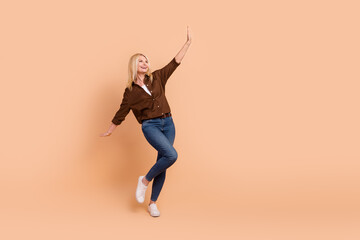 Fototapeta na wymiar Full length body photo of overjoyed middle age woman raise hands dancing delighted isolated beige color background