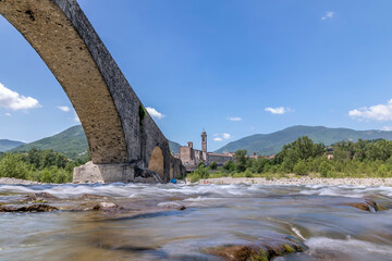 The water of the Trebbia river flows under the Gobbo bridge in Bobbio, Italy, on a hot summer day
