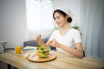 Obraz na płótnie Canvas Happy beautiful Asian woman eating healthy food with vegan.salad in the kitchen at home.