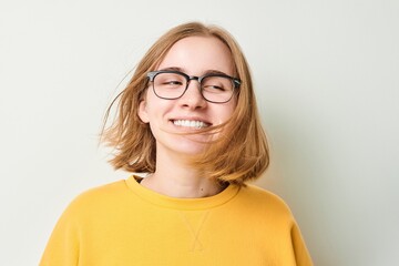Portrait of cute young blond girl in glasses and yellow sweater shakes her head and plays with hair isolated on white studio background