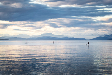 A group of paddle boarders floating across calm water along the Gulf Islands overlooking the Sunshine Coast at background at Miracle Beach Vancouver Island Canada.