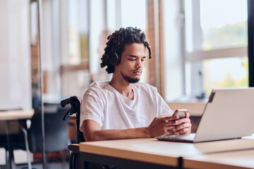 An African American businessman in a wheelchair takes a work break, using his smartphone while...
