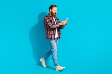 Full length size photo of satisfied red hair man walking texting coworkers while street rest going isolated on blue color background - obrazy, fototapety, plakaty