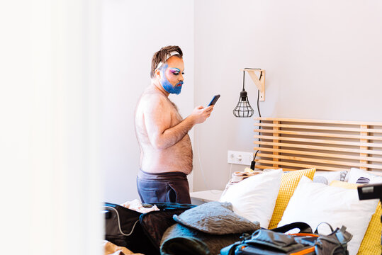 Shirtless man in makeup using smartphone at home - Powered by Adobe