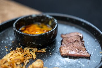 Beef tongue meat served on plate with fried garlic and egg yolk.