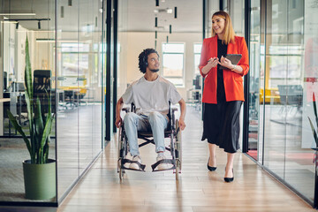 A group of young business people in a modern glass-walled office captures the essence of diversity and collaboration, while two colleagues, including an African American businessman in a wheelchair