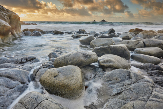 Atlantic rollers surge around shoreline granite boulders on a rising tide at sunset, Porth Nanven, a remote cove near St. Just, in the far west of Cornwall, England, United Kingdom