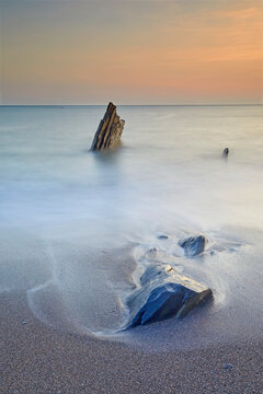 Surf rolls around shoreline rocks at sunset, in Ayrmer Cove, a remote cove near Kingsbridge, south coast of Devon, England, United Kingdom