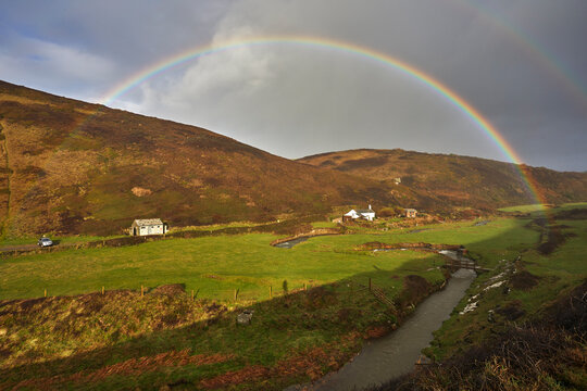 A valley rainbow forms in the face of an autumn squall, in Duckpool, a remote cove near Bude, north coast of Cornwall, England, United Kingdom