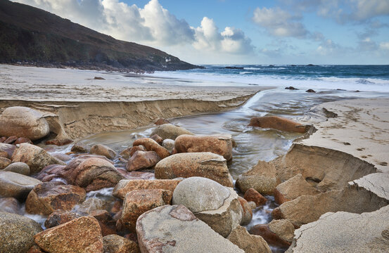 A stream cuts through sand and rocks as it makes its final dash to the sea, Portheras Cove, a remote cove on the Atlantic Coast, near Pendeen, in the far west of Cornwall, England, United Kingdom