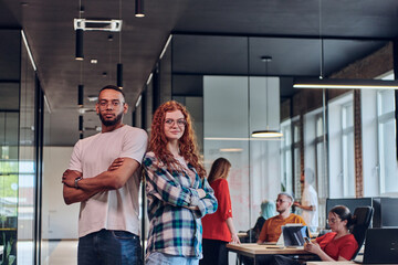 A young African American businessman and a modern businesswoman with orange hair stand side by side, arms crossed, exuding confidence and unity in a contemporary office setting, epitomizing dynamic