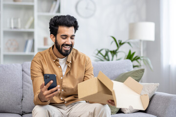 Joyful man at home on the sofa received a package, Latin American is satisfied with the purchase in...