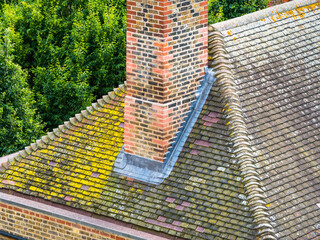 A chimney stack with new lead flashing. Roof tiles aged with moss and yellow lichen. Concept...