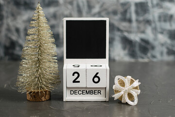 Wooden calendar with December 26 date and beautiful Christmas decoration on dark textured background with copy space