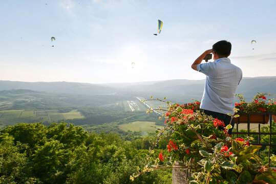 A tourist photographs paragliders from atop the hilltop village of Motovun, Istria, Croatia