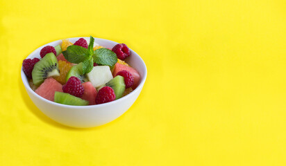 Fruit  salad in the white  bowl on the yellow background. Copy space.